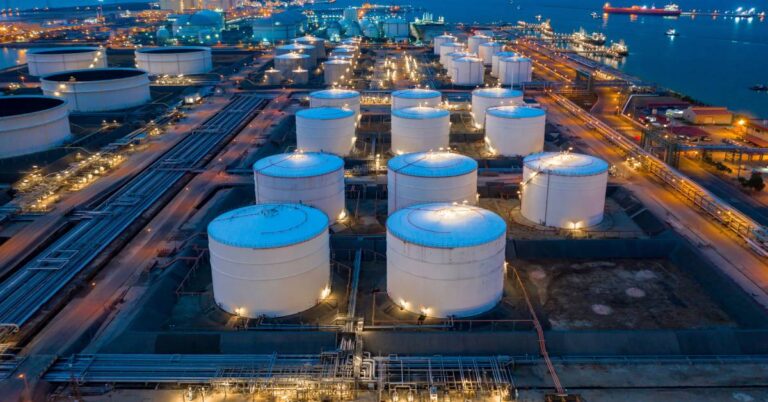 A tank farm from above at night. Multiple oil and gas storage tanks sit next to a large body of water.