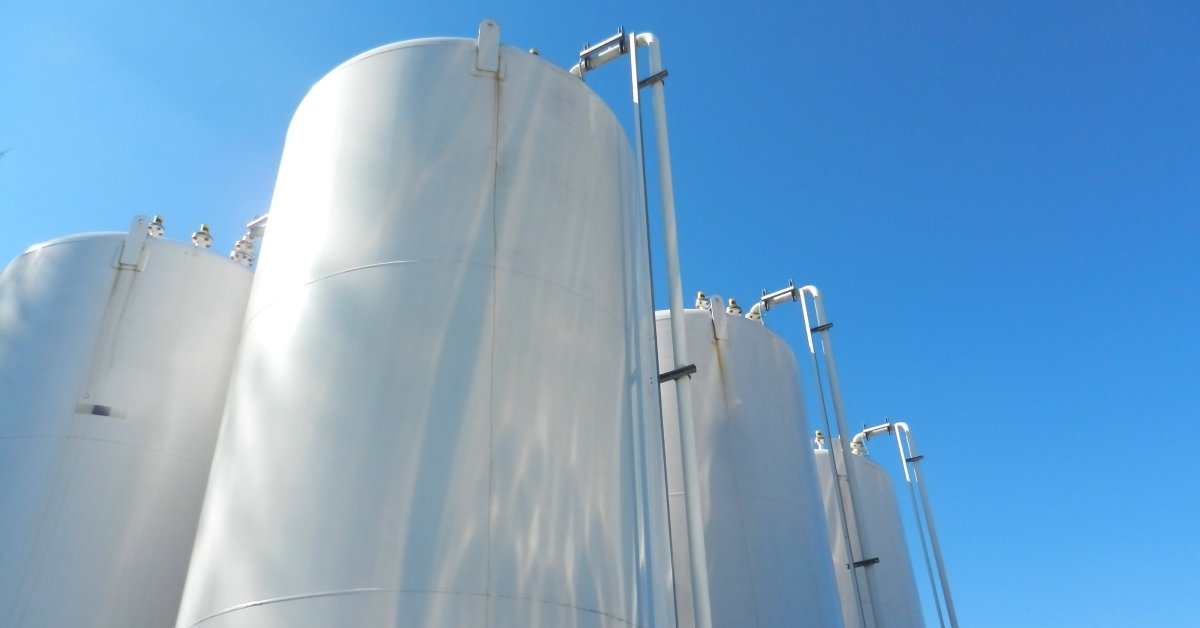 A close-up view of large chemical storage tanks sitting out in the open with the bright blue sky behind them.