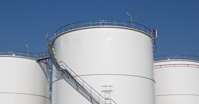 Some large white fuel storage tanks stand next to each other. There's a staircase going around the central tank.