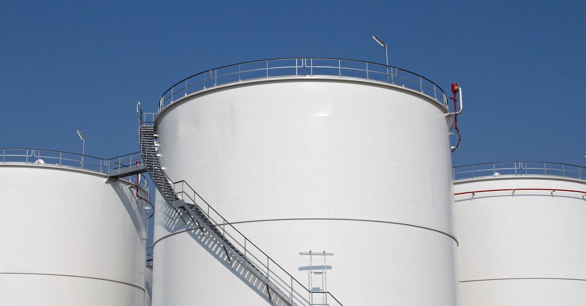 Some large white fuel storage tanks stand next to each other. There's a staircase going around the central tank.