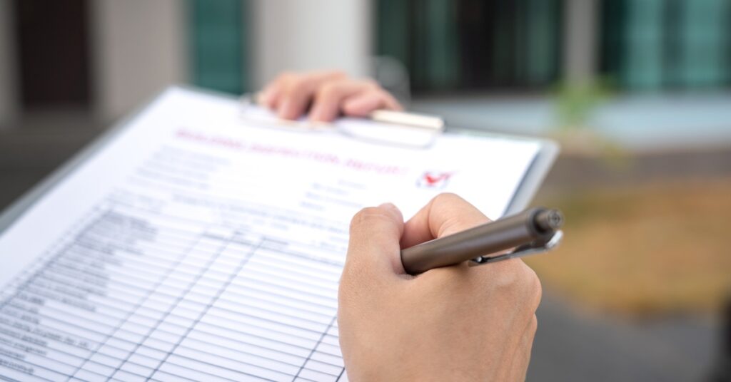 A close up of someone holding a clipboard with their left hand and filling out a form on the clipboard in with their right hand.
