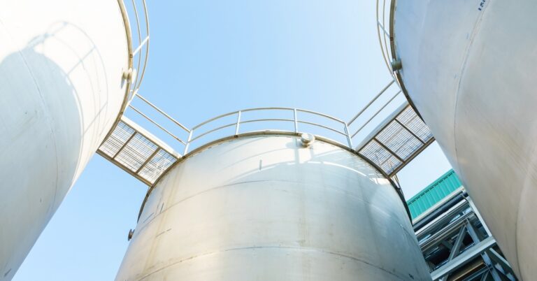 Multiple large storage tanks stand next to each other, connected by small bridges, with an empty sky in the background.