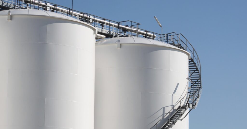 Two large storage tanks sit next to each other with a large black staircase running around the tank on the right.
