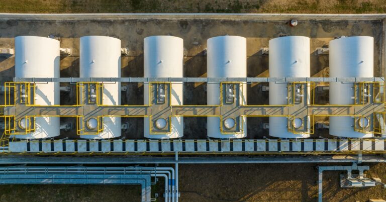 An aerial view of six large storage tanks sitting next to each other with large pipes connecting them.