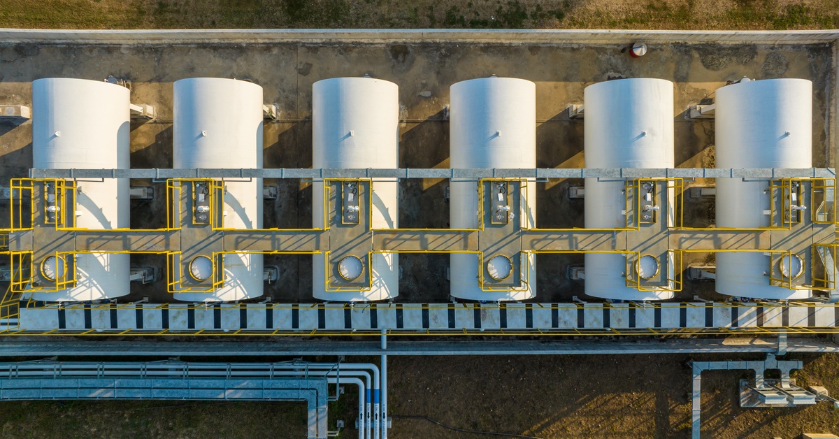 An aerial view of six large storage tanks sitting next to each other with large pipes connecting them.