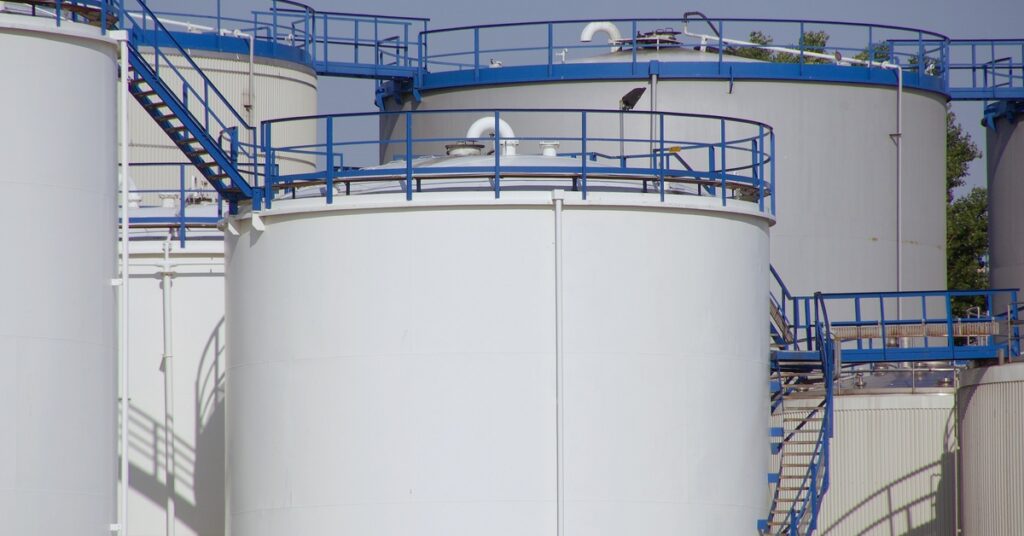 Multiple storage tanks standing next to one another, each connected by stairs and bridges with blue railings.