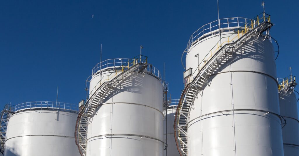 Some large industrial white storage tanks standing tall next to each other with staircases going around them.