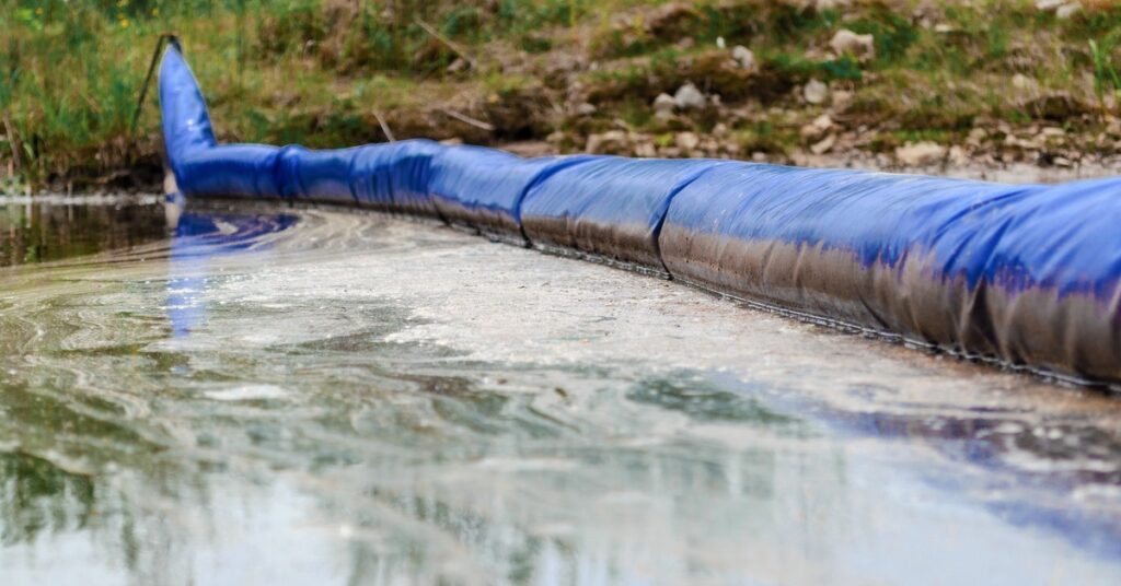 A barrier in a body of water helps to separate an oil spill that is spreading. The barrier is blue with vegetation on the side.