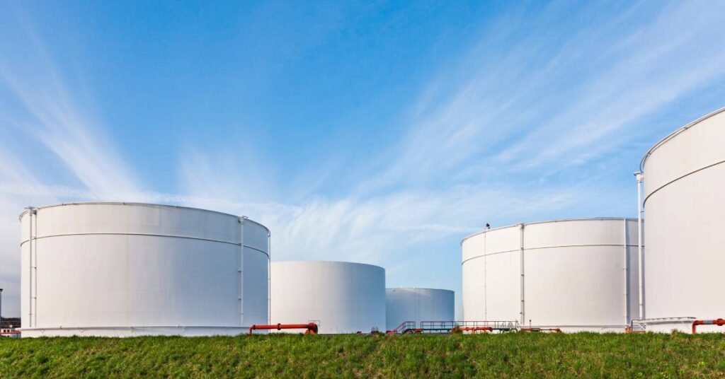 A large farm with multiple white storage tanks standing next to each other, connected by red pipes.
