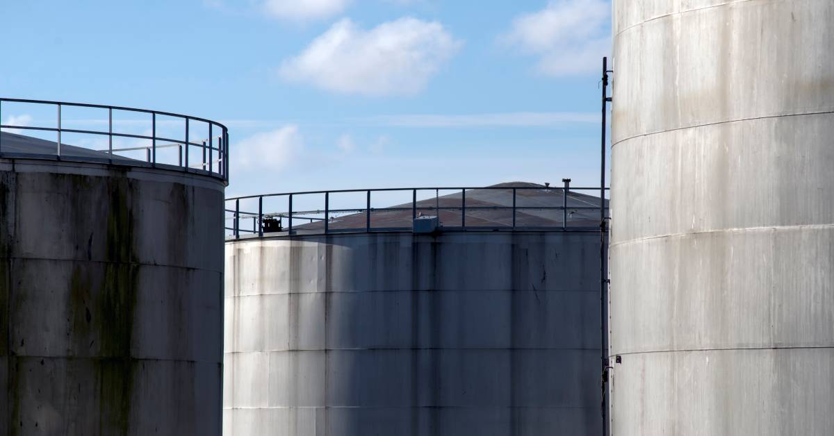 Three large industrial storage tanks standing next to each other. Each tank is tall and there is railing at the top.