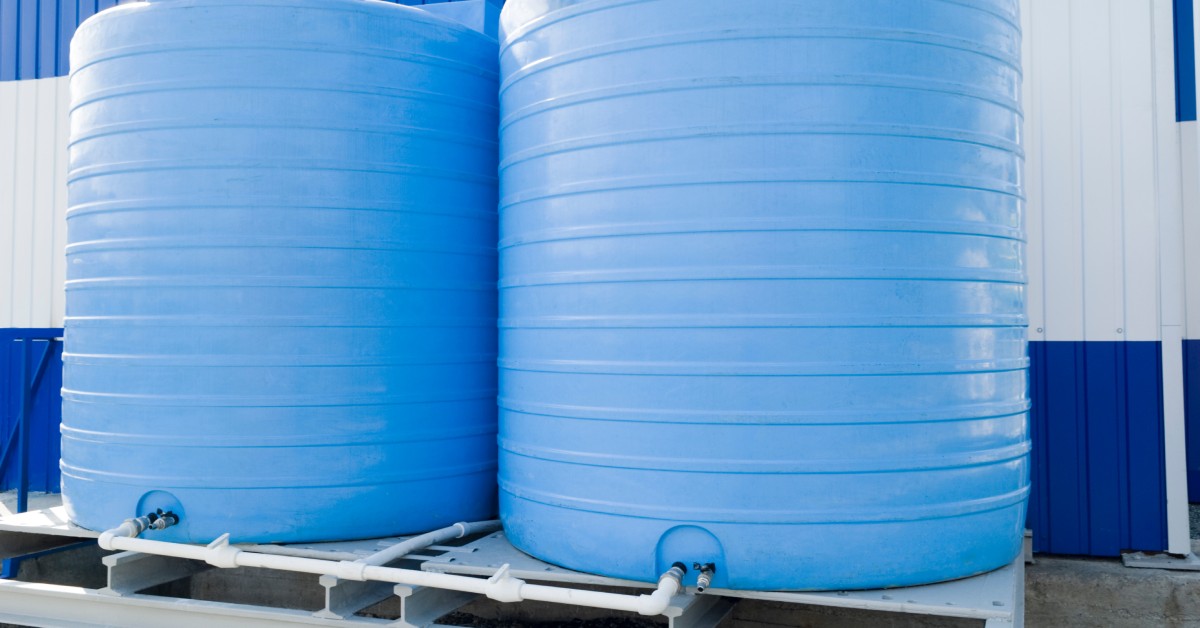 Two large blueish cisterns sitting next to each other on a platform. They are connected to each other by a small pipe.