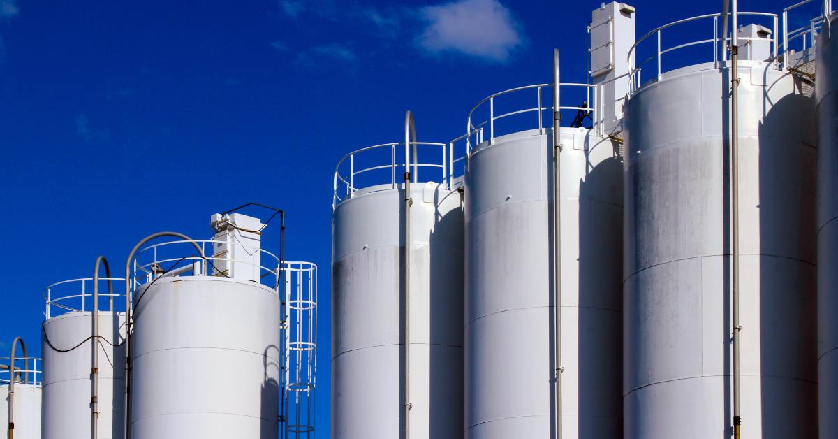 Large, tall cylindrical storage tanks standing next to each other against a dark blue sky with some clouds.