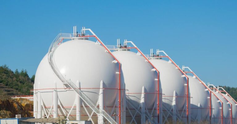 Large spherical storage tanks standing next to each other in a large empty field. The tanks have orange pipes connecting them.
