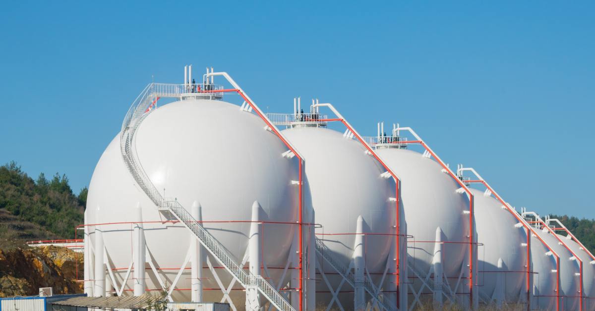 Large spherical storage tanks standing next to each other in a large empty field. The tanks have orange pipes connecting them.