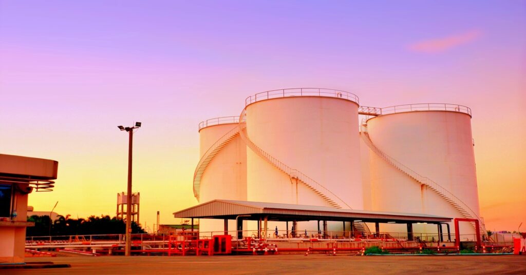 Four large shite storage tanks standing next to each other at a facility while the sun sets behind them.