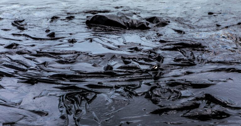 A massive black chemical spill liner during the daytime. The liner is completely covered in a liquid.