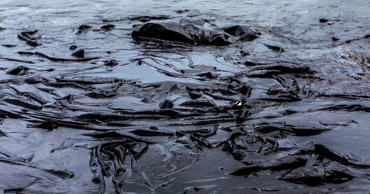 A massive black chemical spill liner during the daytime. The liner is completely covered in a liquid.
