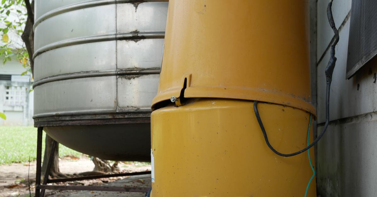 A small, broken yellow tank next to a larger metal tank outside a building. Both have wear and tear.