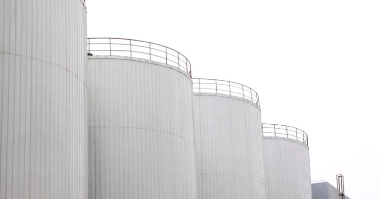 Four white, metal water tanks lined up against an industrial building under a white, overcast sky.