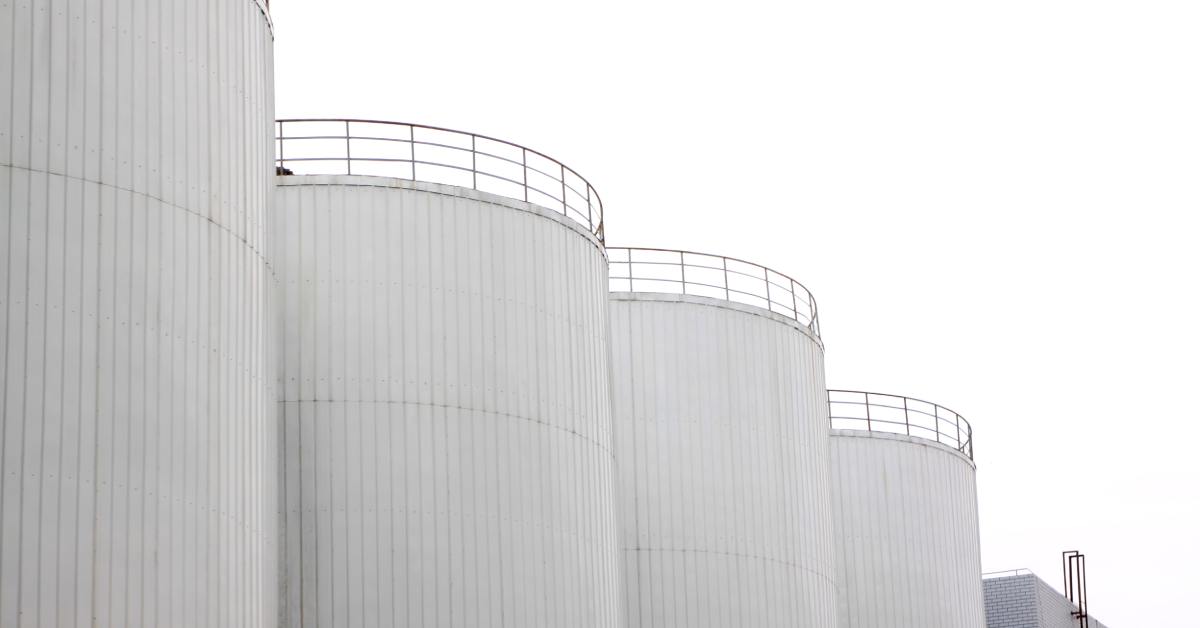 Four white, metal water tanks lined up against an industrial building under a white, overcast sky.