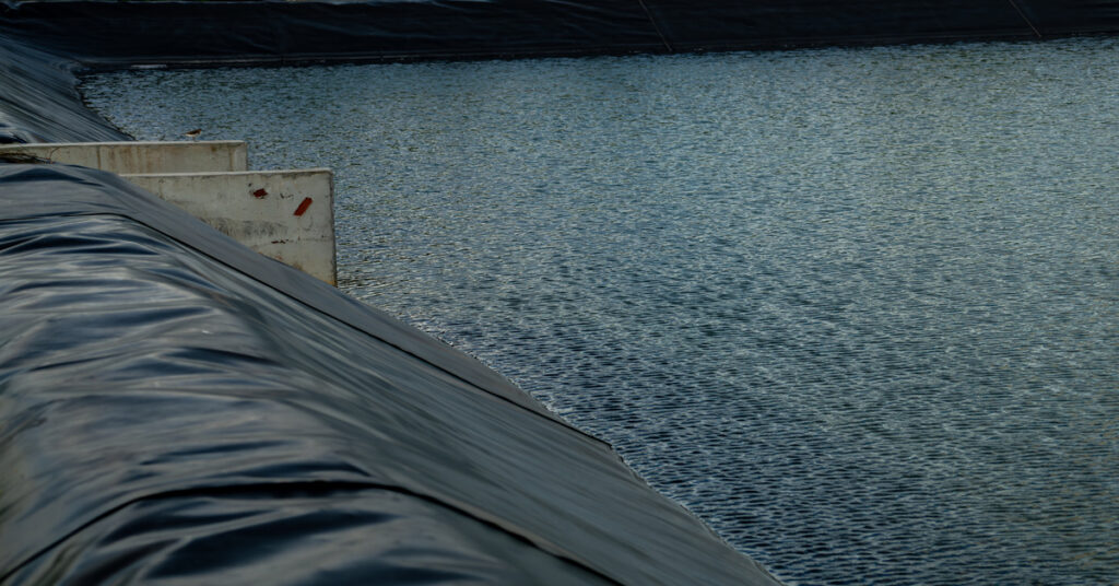 A black water treatment pond liner stretches over the side of a large water enclosure, lining the sides around the structure.