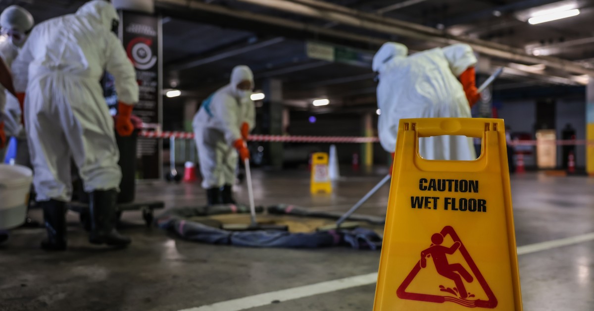 A crew in hazmat suits cleaning up a chemical spill and a sign that reads "Caution Wet Floor" in the foreground.
