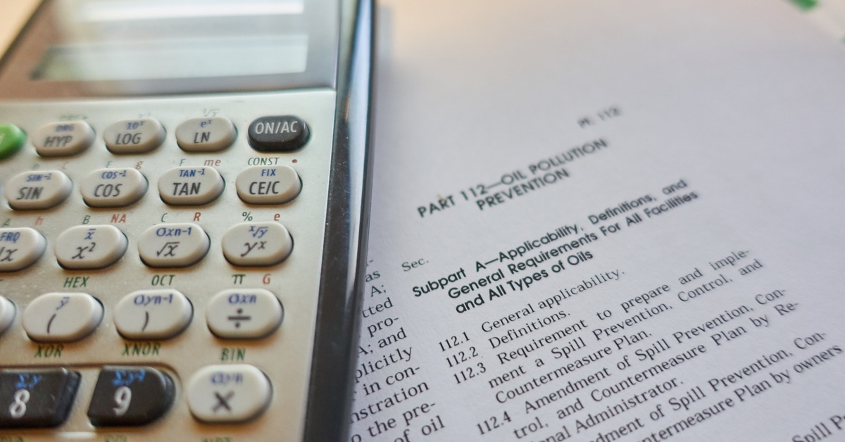 A close-up of a calculator resting on a document with federal regulations for oil pollution prevention.