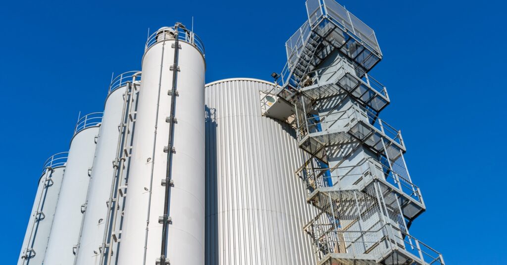 A ground-up shot of a tall industrial tank tower with stairs leading up to it and several other towers on the side.