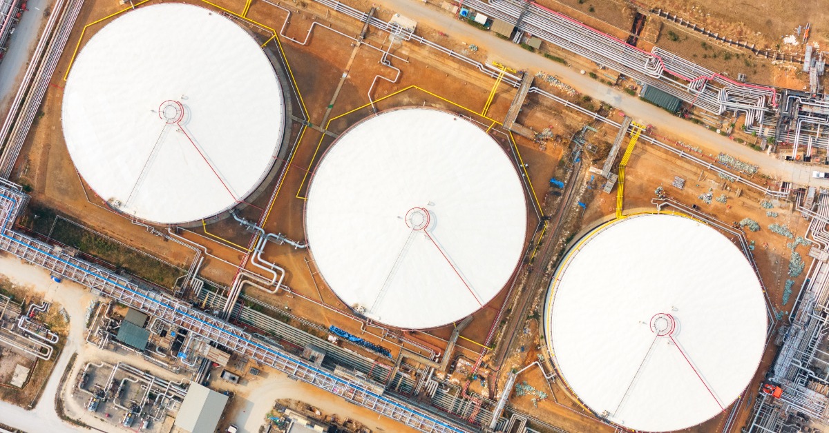 Three white oil storage tanks surrounded by pipelines, roads, and equipment across a brown industrial facility.